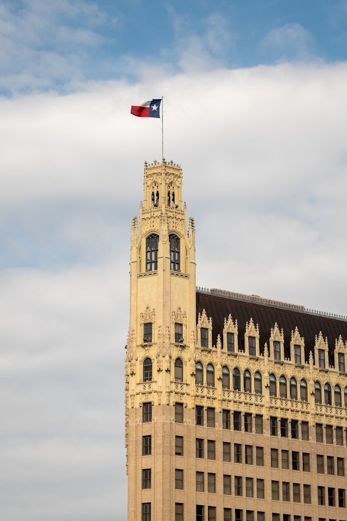 Iconic historic tower topped with Texas flag under a blue sky.